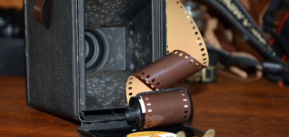 Eine alte Kamera die an der Rückseite geöffnet ist und aus der eine Filmrolle heraus kommt