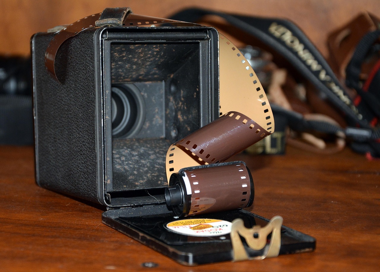 Eine alte Kamera die an der Rückseite geöffnet ist und aus der eine Filmrolle heraus kommt