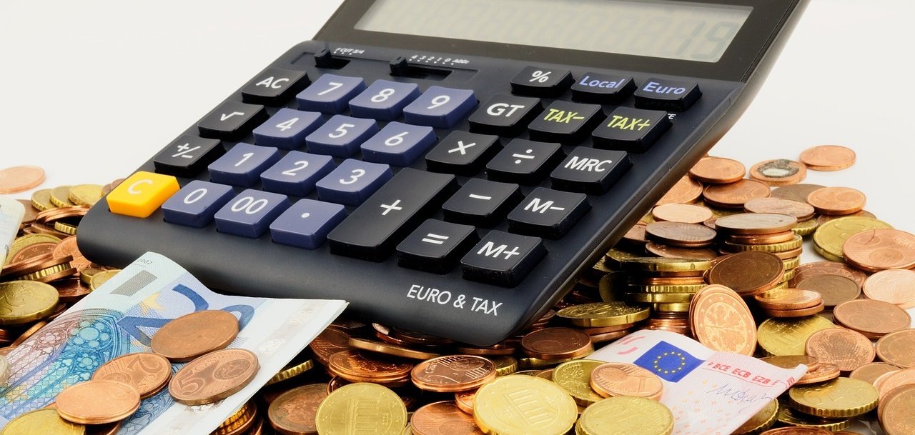 Eine Anhäufung von Münz- und Scheingeld auf der ein Taschenrechner liegt 