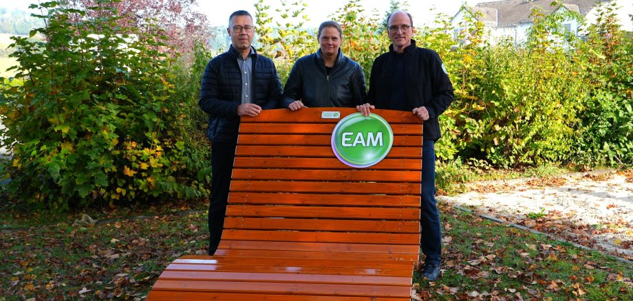 Sitzbank der EAM neben dem Rathaus Hinter der Bank stehen, von links, Andreas Glatthaar (Erster Beigeordneter), Christine Nadler (Fachbereichsleiterin Hochbau/Bauverwaltung), Marcus Hief (Leiter der EAM Netzregion Dillenburg)