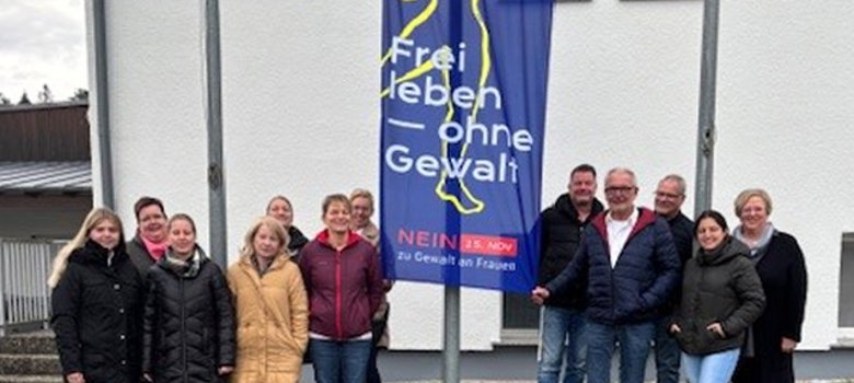 Mitarbeiterinnen und Mitarbeiter der Verwaltung vor dem Rathaus mit der Flagge zur Aktion "Frei leben ohne Gewalt"