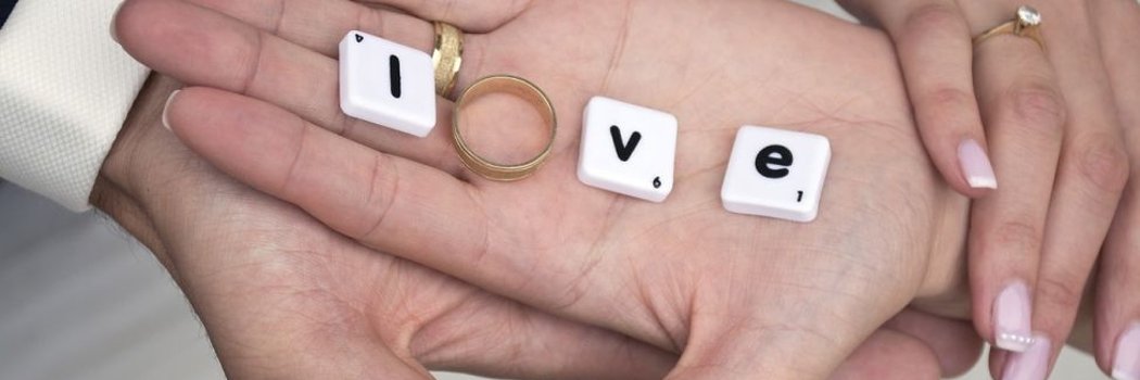 Zwei Hände in denen Scrabblesteine und ein Ring das Wort Love bilden
